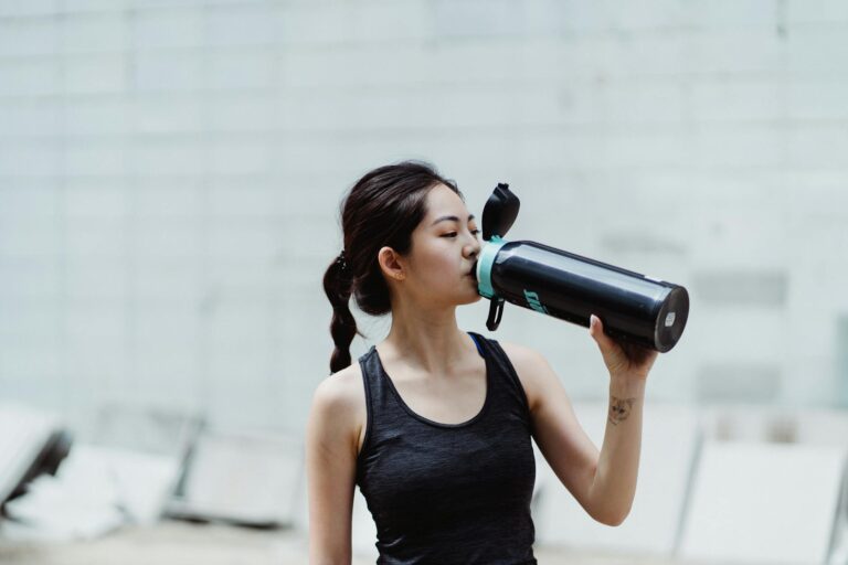 Young woman in workout attire drinks from a water bottle, promoting healthy lifestyle.