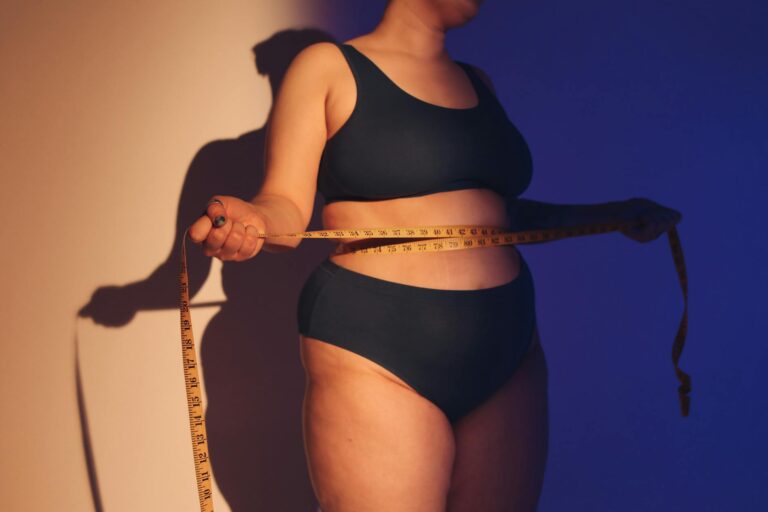 A woman in underwear measures her waist with a tape measure, embracing body positivity.