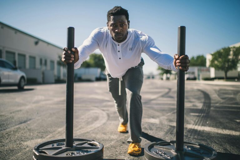 Man in athletic wear pushing sled outdoors, showcasing strength and determination.