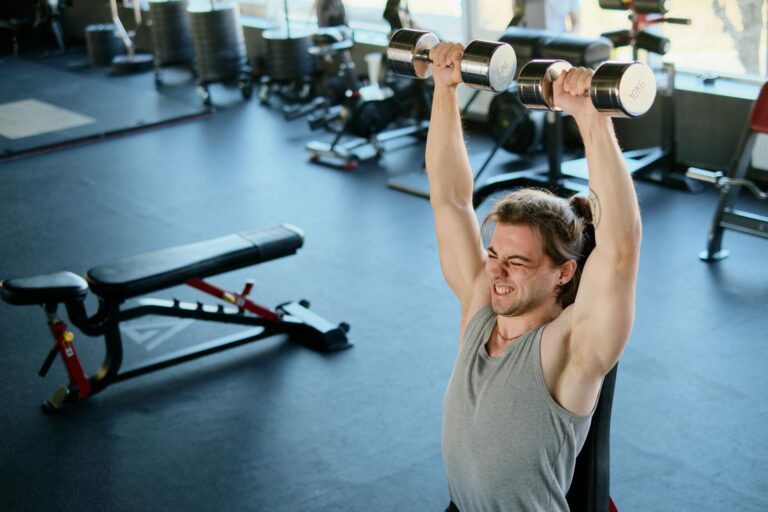 Man intensely lifting dumbbells in a modern gym, showcasing strength and endurance.
