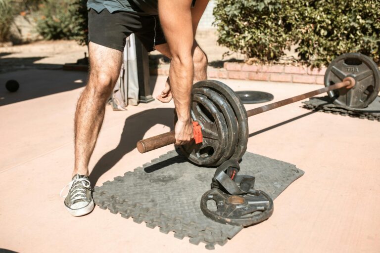 Man lifting barbell outdoors on a sunny day, focusing on workout and fitness.