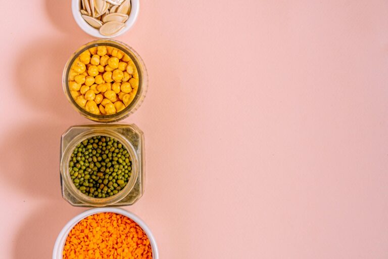 Flat lay of chickpeas, lentils, mung beans, and pumpkin seeds with pink backdrop.