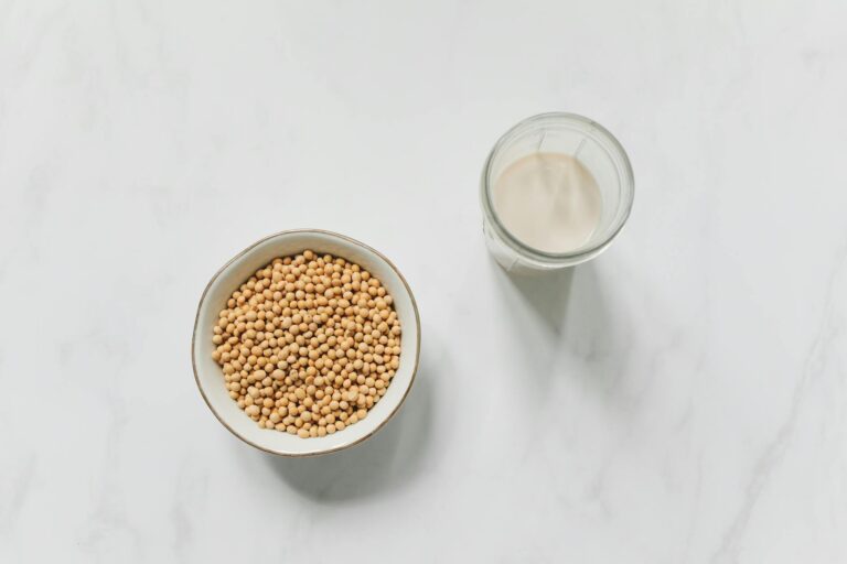 Bowl of soybeans and a glass of soy milk placed on white marble surface.