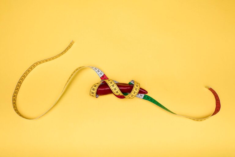 A red pepper wrapped in a colorful measuring tape, set against a bright yellow backdrop, symbolizing health and measurement.