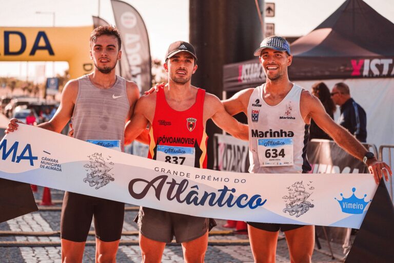 Three marathon runners celebrate their victory at the Grande Prémio do Atlântico in bright outdoor conditions.