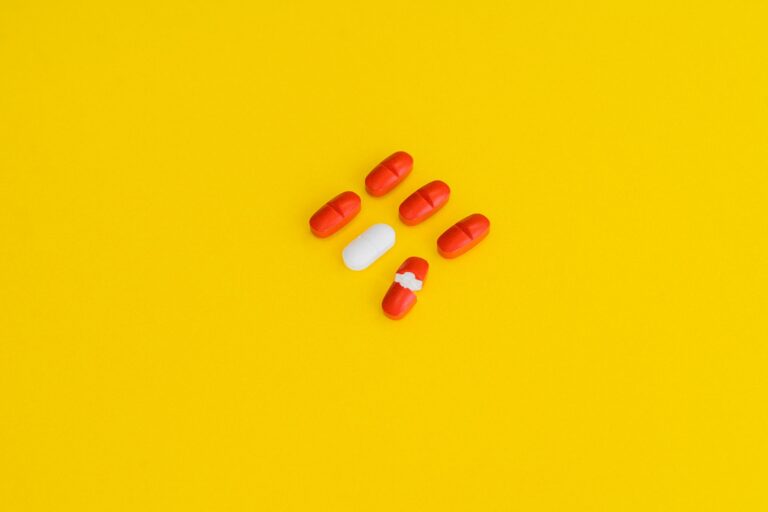 Red capsules and a white tablet arranged on a bright yellow surface, symbolizing healthcare.