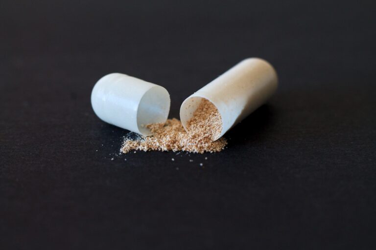 Close-up of a split capsule with powder spilling on a dark surface, symbolizing medicine and health.