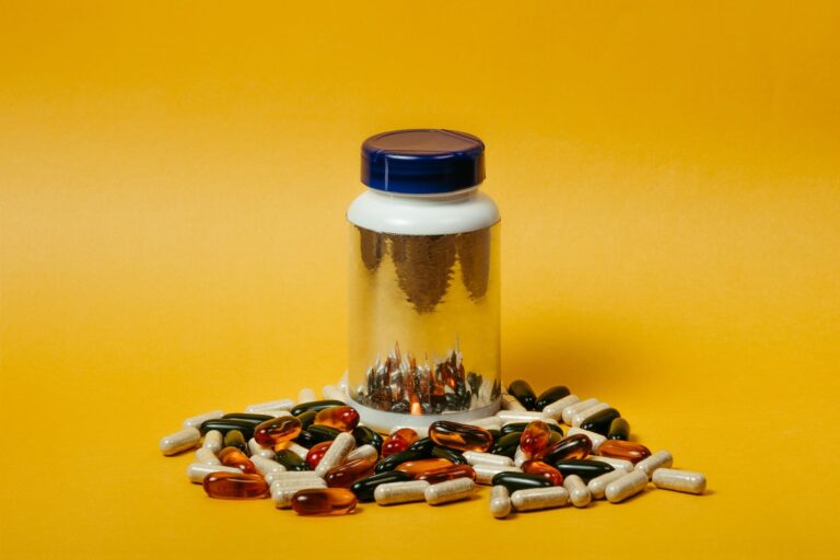 Vibrant collection of multi-colored pills and capsules surrounding a reflective pill bottle on a bright yellow background.