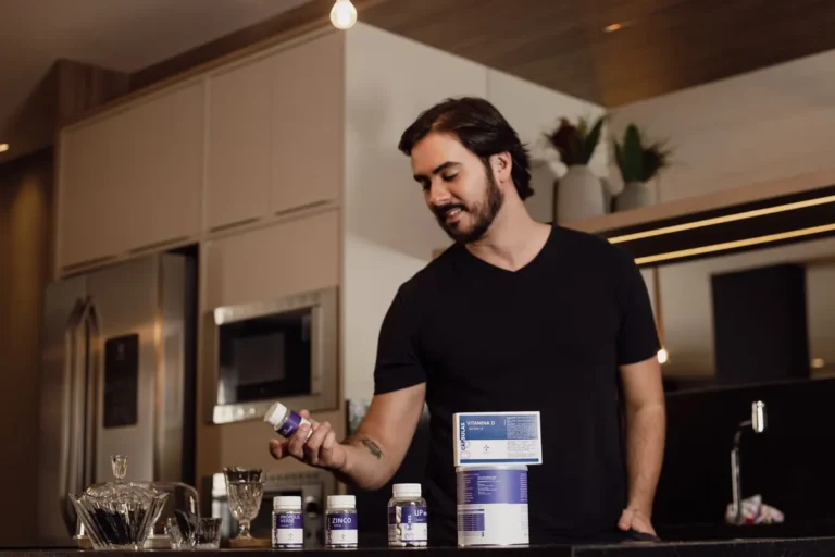 Man in a modern kitchen holding a vitamin supplement bottle, surrounded by health products.