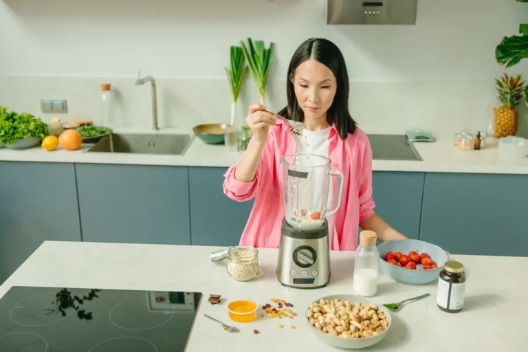 A woman in a kitchen preparing a nutritious smoothie with fresh ingredients.