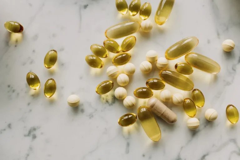A variety of capsules and pills scattered on a light marble background.